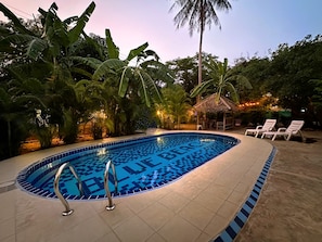 Una piscina con un diseño de azulejos azules y blancos, rodeada de exuberante follaje y palmeras.