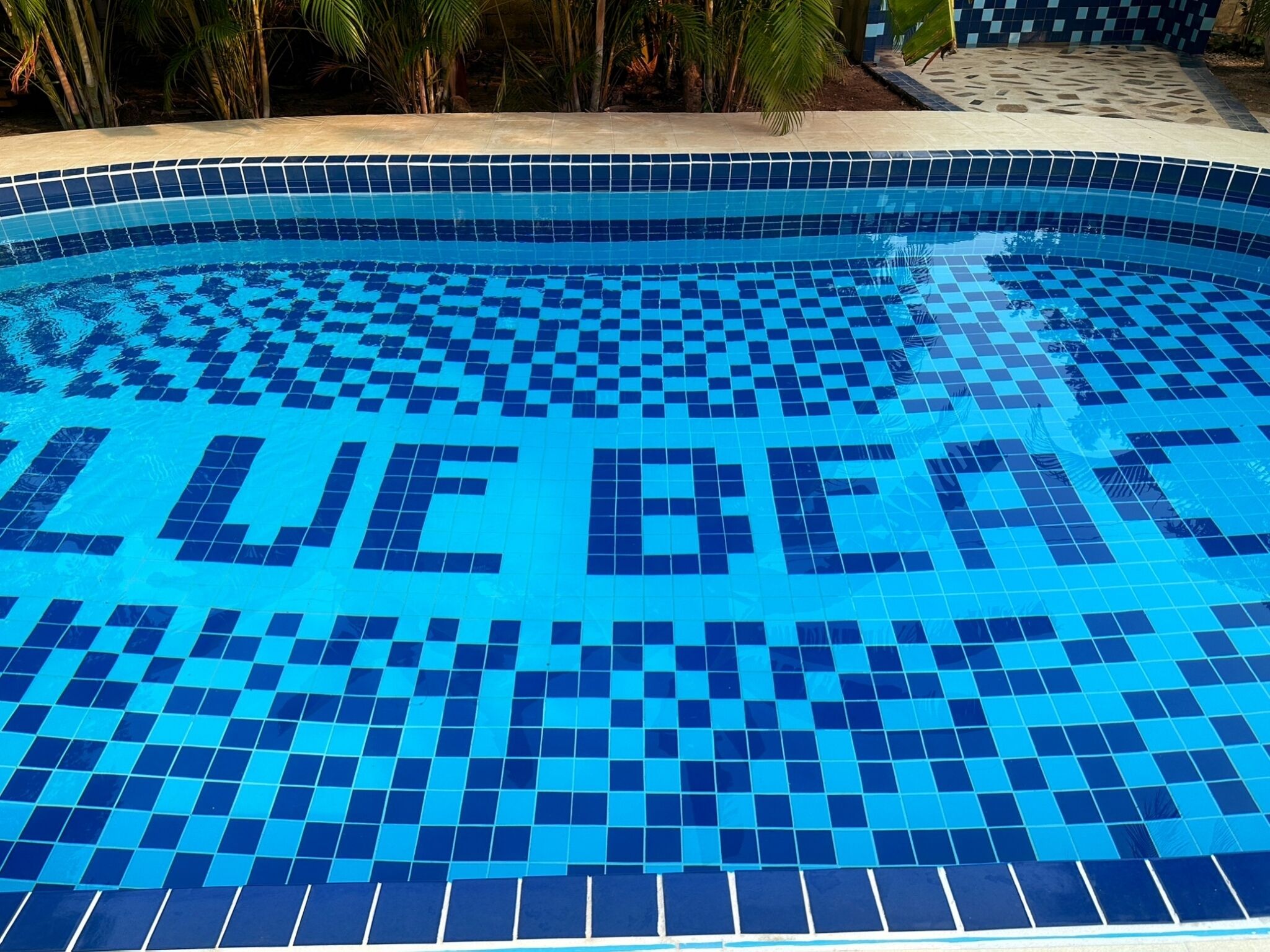 A swimming pool with a checkered tile pattern and the words "BLUE BEACH" written on the tiles.