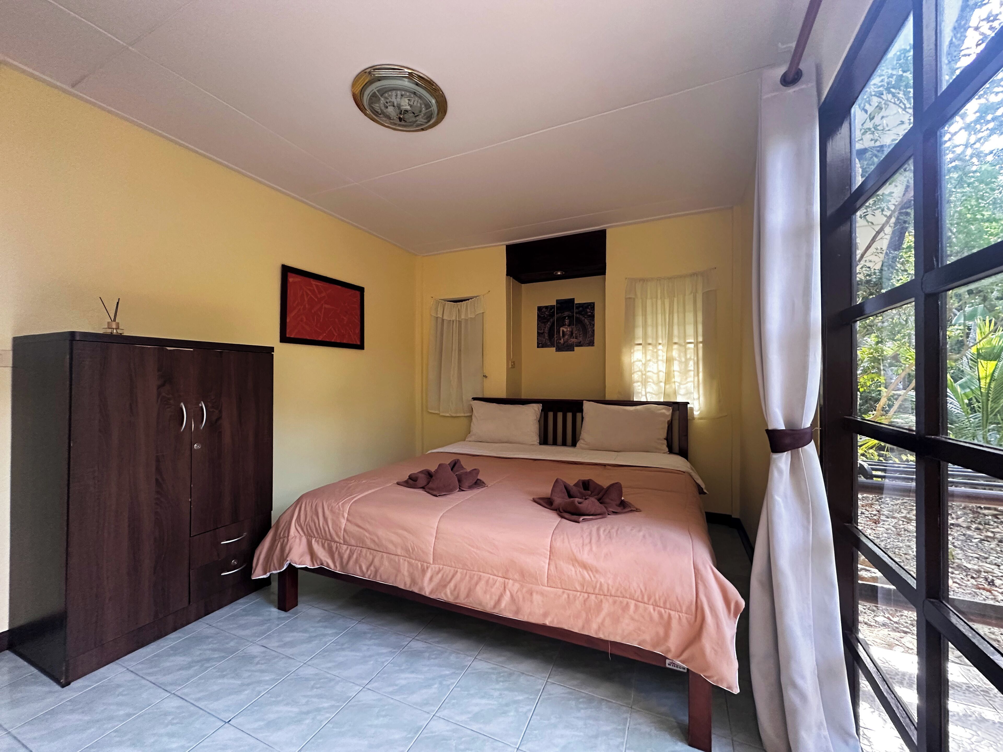 Un dormitorio con cama, armario, lámpara en el techo, ventana con cortinas e imagen colgada en la pared.