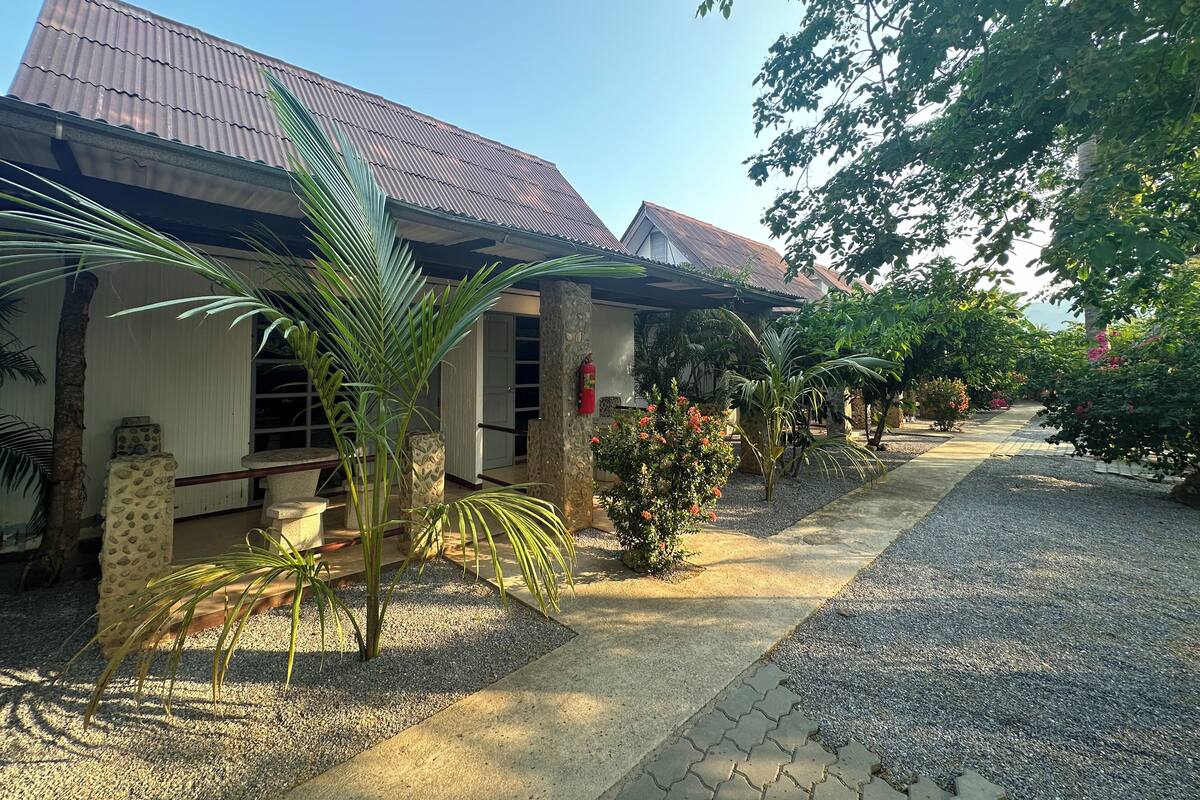 A house with a corrugated metal roof, a stone pillar, and a gravel pathway leading to the entrance.