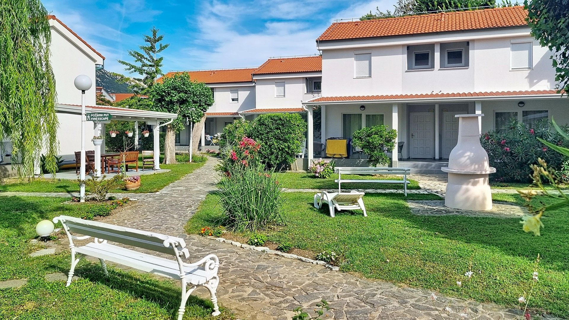 A courtyard with a white bench, a stone pathway, and a covered seating area.