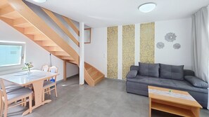 Un salon moderne avec un canapé gris, un escalier en bois et un coin repas comprenant une table et des chaises.