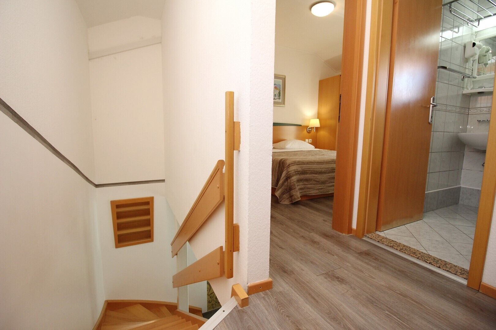 Una escalera conduce a un dormitorio con cama, un baño con ducha y una puerta de madera.