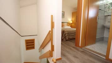 Una escalera conduce a un dormitorio con cama, un baño con ducha y una puerta de madera.