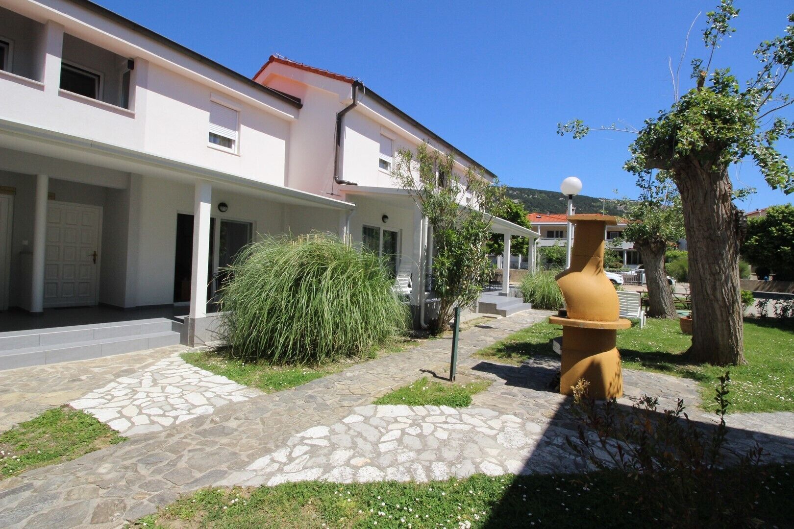 Un moderno edificio de dos pisos con entrada empaveda de piedra y un gran jarro decorativo.