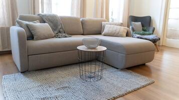 Un salon moderne avec un canapé d’angle beige, une table basse ronde surmontée d’un bol en fibres tressées et un tapis à motifs.