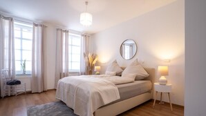 Ein Schlafzimmer mit Bett, Nachttischlampen, einem Spiegel und einem Fenster mit Vorhängen.