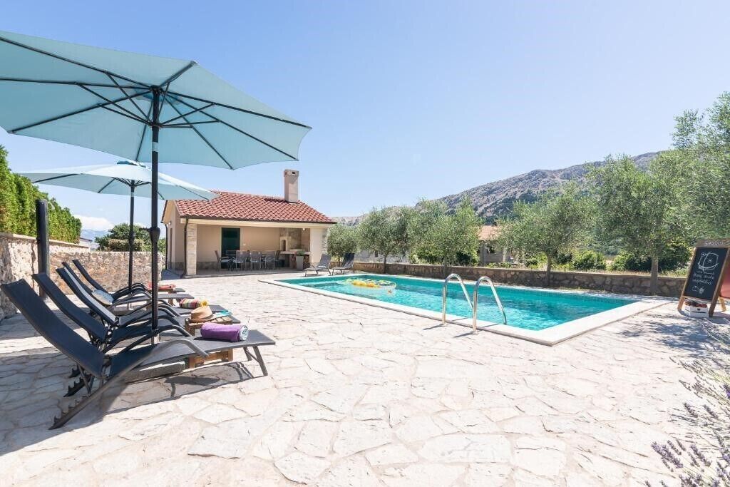 A pool area with lounge chairs and umbrellas, a stone floor, and a view of the surrounding landscape.