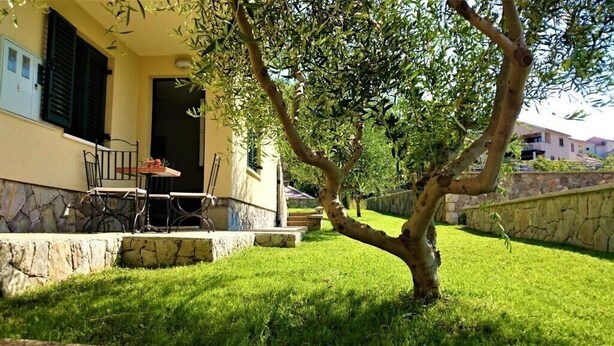 Una casa con un pequeño patio, una mesa y sillas. Un árbol se encuentra frente a la casa.