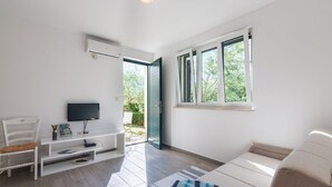 Un salon moderne avec un téléviseur, des meubles blancs, un canapé et une grande fenêtre.