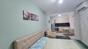 A bedroom with a bed, a sofa, and a kitchenette in the background.