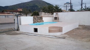 A swimming pool with a stone wall and a small opening, surrounded by a concrete area and a metal gate.
