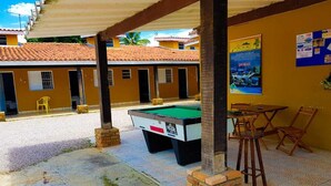 An outdoor pool area with a pool table, chairs, and a brick wall.