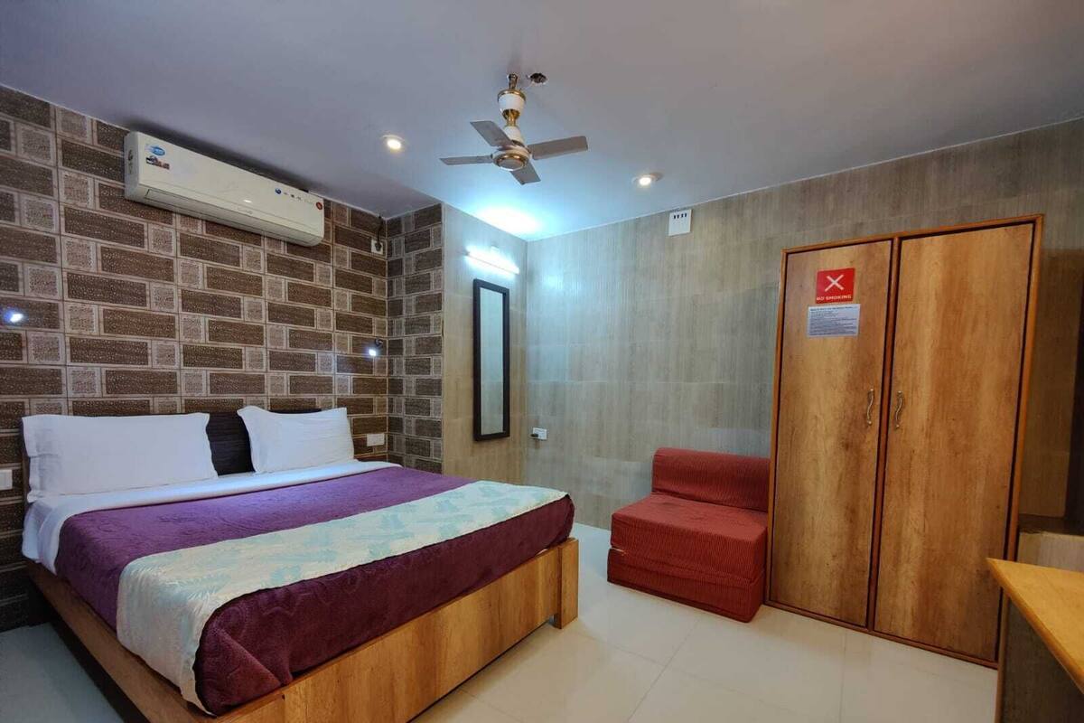 A bedroom with a bed, a red chair, a wardrobe, and a ceiling fan.
