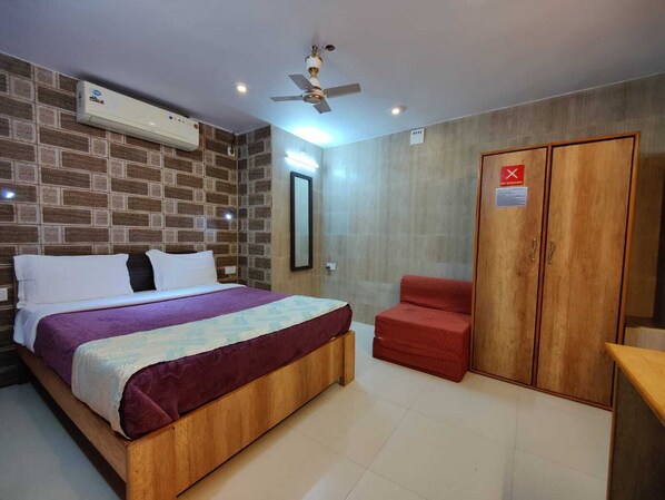A bedroom with a bed, a red chair, a wardrobe, and a ceiling fan.