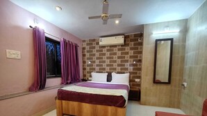 A bedroom with a wooden bed, purple curtains, a brick-patterned wall, an air conditioning unit, and a ceiling fan. - Aditya Forest Eco Resort (Abu Road)