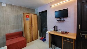 A small room with a wooden wardrobe, a red sofa, a desk with a television, and a door with a 'No Smoking' sign. - Aditya Forest Eco Resort (Abu Road)
