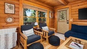 Een gezellig cabin interieur met houten wanden, een blauwe bank, twee geruite fauteuils, een houten salontafel en een kaart aan de muur.