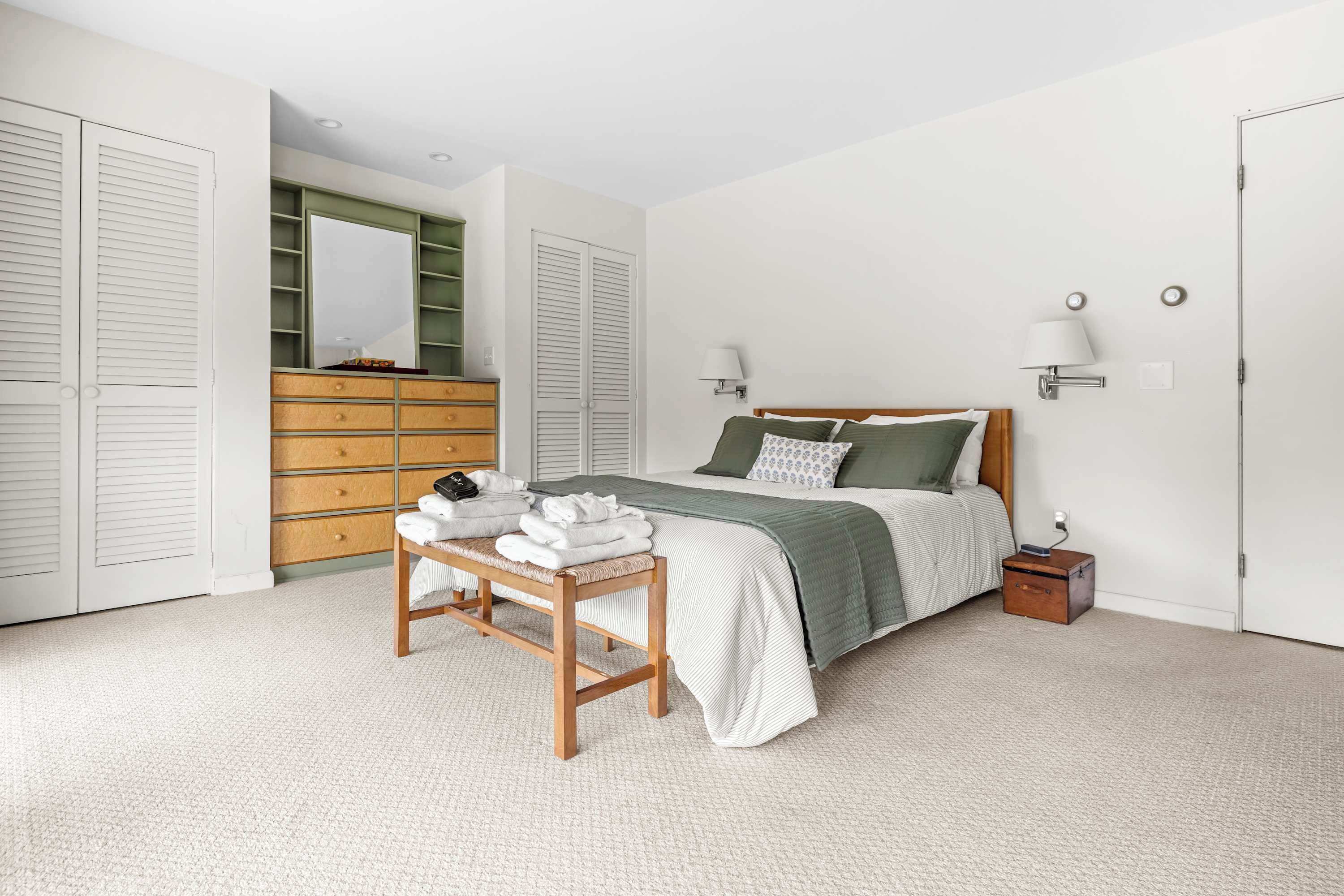 Un dormitorio con cama, mesitas de noche, cómoda y espejo.