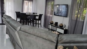 En moderne stue med en grå sofa, et spisebord med stole, et fjernsyn monteret på væggen og et lille sofabord med pynteting.