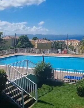 Une piscine avec vue sur la mer, entourĂ©e dâune zone dĂ©limitĂ©e par une clĂŽture et de verdure.