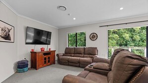Un salon avec un canapé en cuir marron, un meuble de rangement en bois, un téléviseur à écran plat et une horloge au mur.