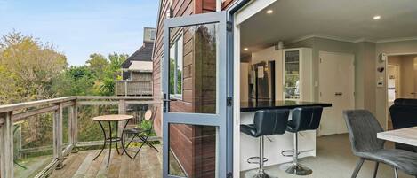 A modern kitchen with a bar area, a dining table with chairs, and a wooden deck.