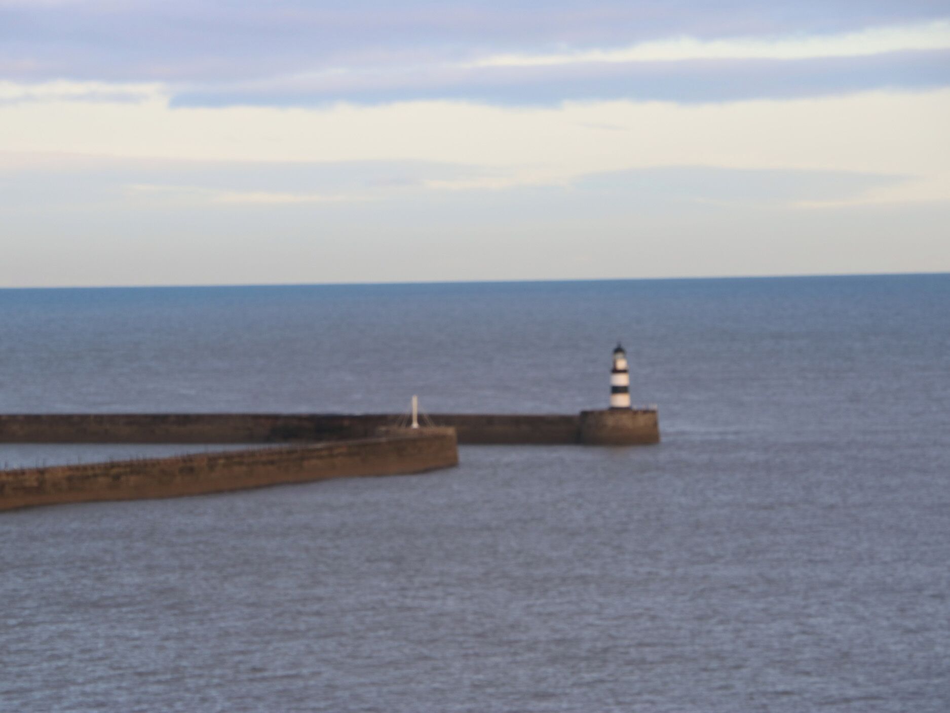 Un faro en un muelle que se adentra en aguas tranquilas.