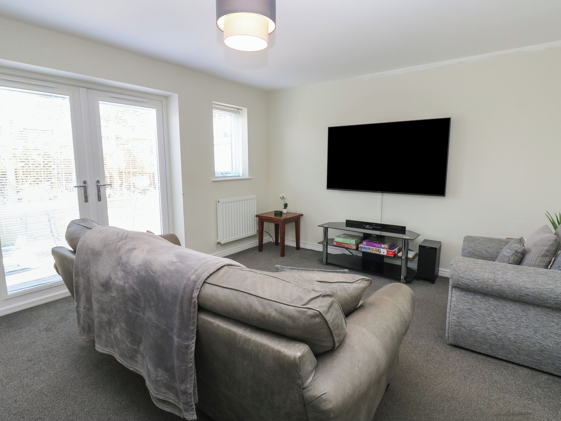 Ein modernes Wohnzimmer mit grauem Sofa, einem grauen Sessel, einem flachbildfernseher an der Wand und einem kleinen Holztisch mit Büchern.