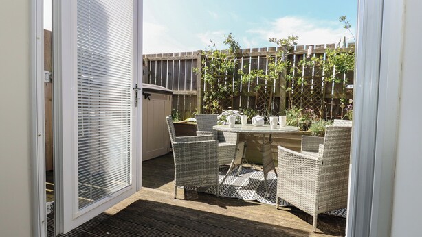 An open sliding glass door leading to an outdoor patio with wicker furniture and a table set for four. - 5 Ashcroft Mews (Seaham)
