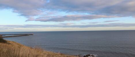 A coastal landscape with a lighthouse, grassy terrain, and a calm sea under a partly cloudy sky.