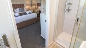 A hotel room with a bed, bedside tables, lamps, a shower area, and a bathroom with a toilet and sink. - 5 Ashcroft Mews (Seaham)