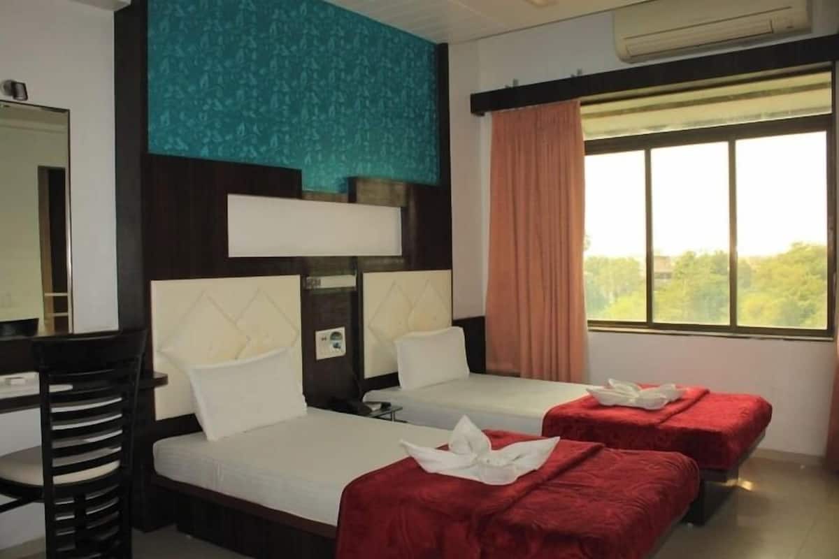 Habitación de hotel con dos camas, un escritorio y ventana con vistas a zonas verdes.
