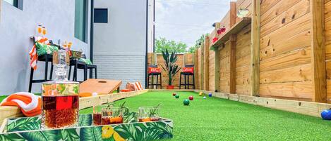 Un jardin avec une pelouse artificielle, une table de ping-pong et un petit espace aménagé avec des plantes en pot.