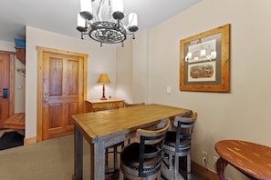 Un comedor con una mesa y sillas de madera, una araña, un cuadro en la pared y una puerta.