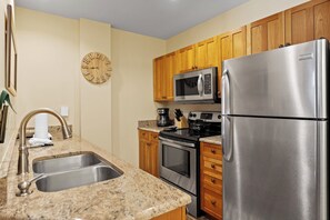 Compact kitchen area with modern amenities, featuring a refrigerator, microwave, oven, sink, and coffee maker.