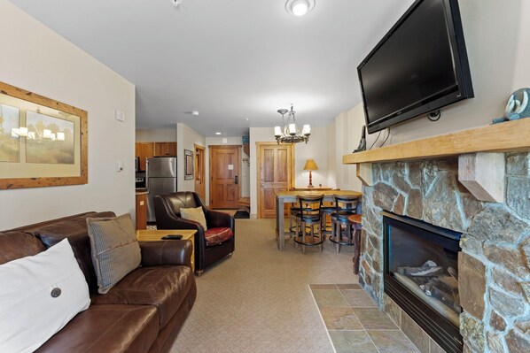 A living room with a stone fireplace, a leather sofa, a television, and a dining area with chairs and a table.