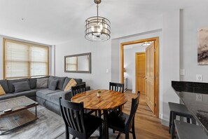 A modern living room with a sectional sofa, a wooden dining table, and a kitchen area with a black countertop. - Prime River Run Location: 2-Min Walk to the Gondola! (Keystone)
