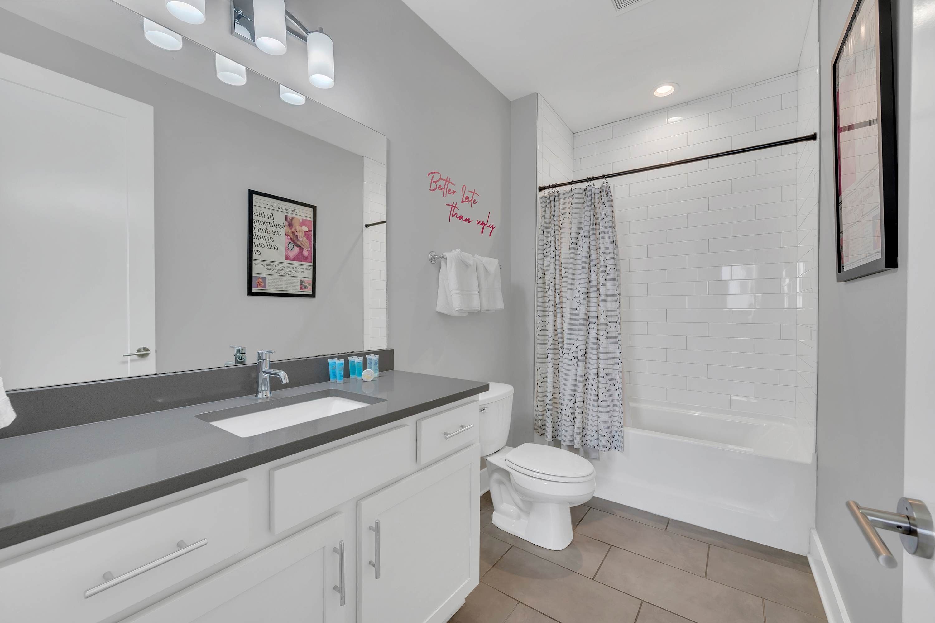 A modern bathroom with a grey and white color scheme, a large mirror, a sink, a toilet, and a shower area.