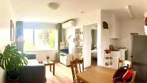 Un espacio habitable compacto con comedor, cocina y un amplio ventanal que proporciona luz natural.