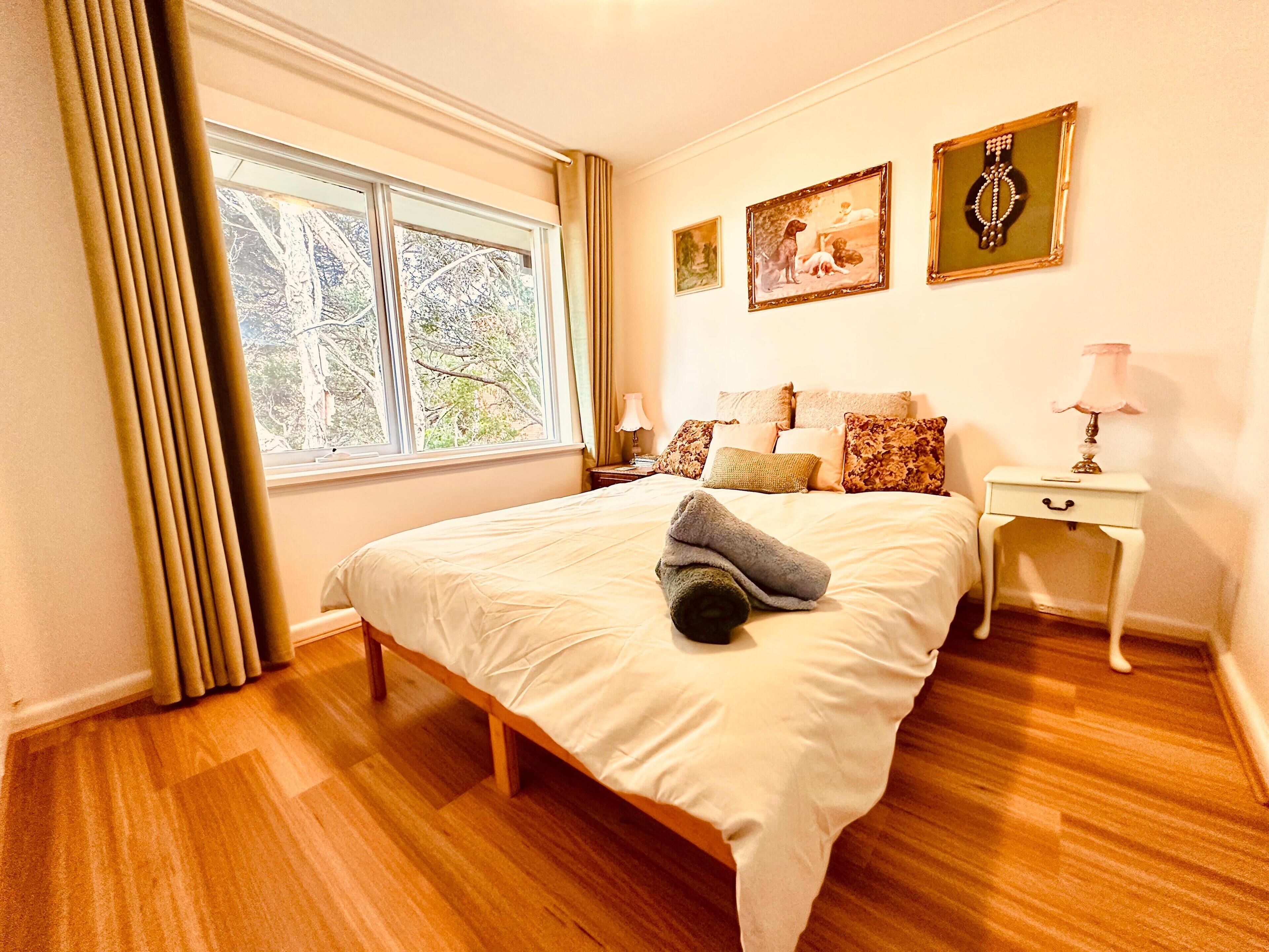 A bedroom with a large bed, a nightstand, a lamp, and two framed pictures on the wall.