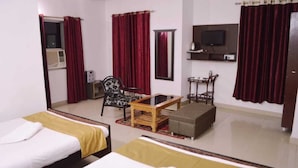 Une chambre d’hôtel avec deux lits, une table basse en bois, une chaise, un téléviseur et une petite table avec une lampe.