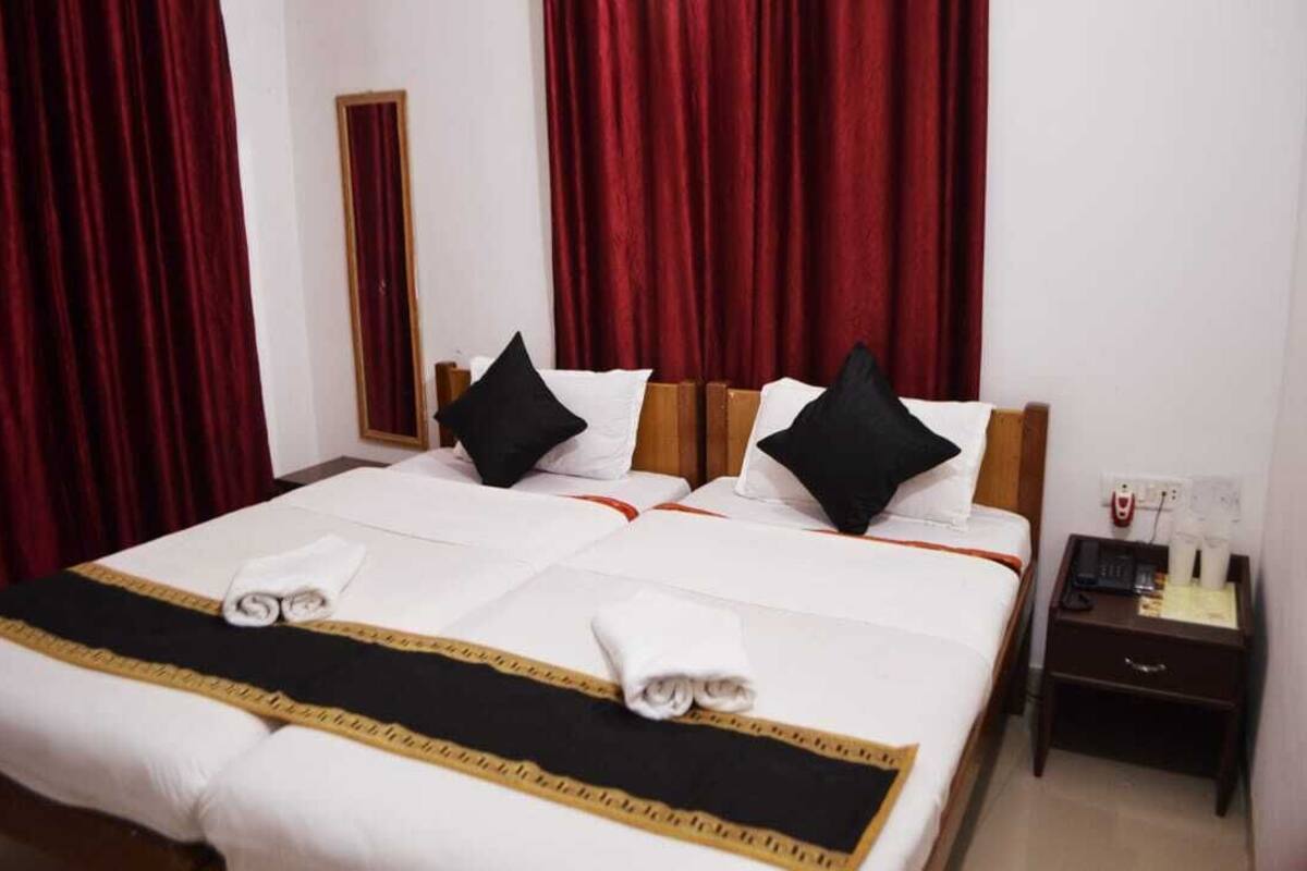 Une chambre d’hôtel avec un grand lit, des rideaux rouges, une tête de lit en bois et une table de chevet avec un téléphone et une lampe.