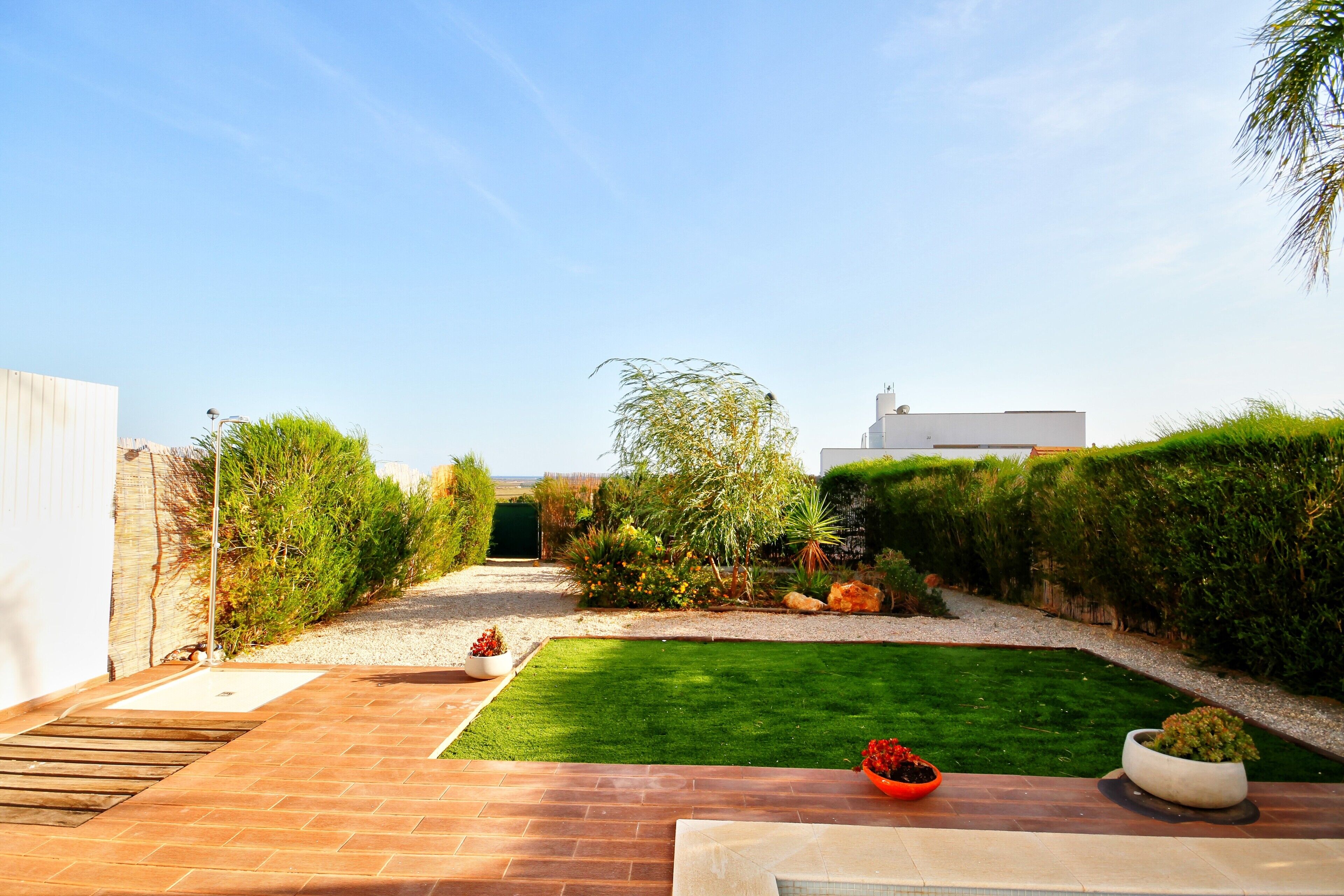 A well-maintained garden with a paved patio, neatly trimmed hedges, and a variety of plants.