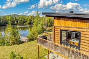 A cabin with a deck overlooking a lake, surrounded by trees.