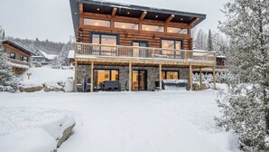 Una cabaña de troncos de varios pisos con un balcón, rodeada de árboles cubiertos de nieve.