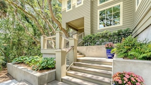 A house with a concrete staircase leading to a covered porch, surrounded by lush greenery and a large potted plant. - Oceanfront, private boardwalk and pool (Kiawah Island)