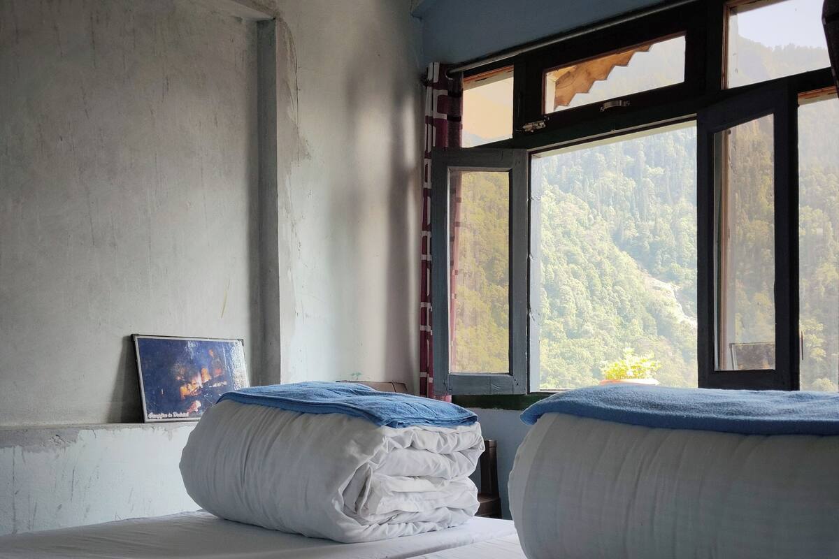 A room with a bed, a window with a view of a forest, and a painting on the wall.