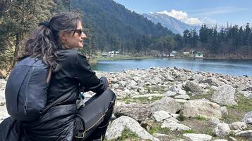 Una persona sentada en una orilla rocosa junto a un lago, con montañas al fondo.