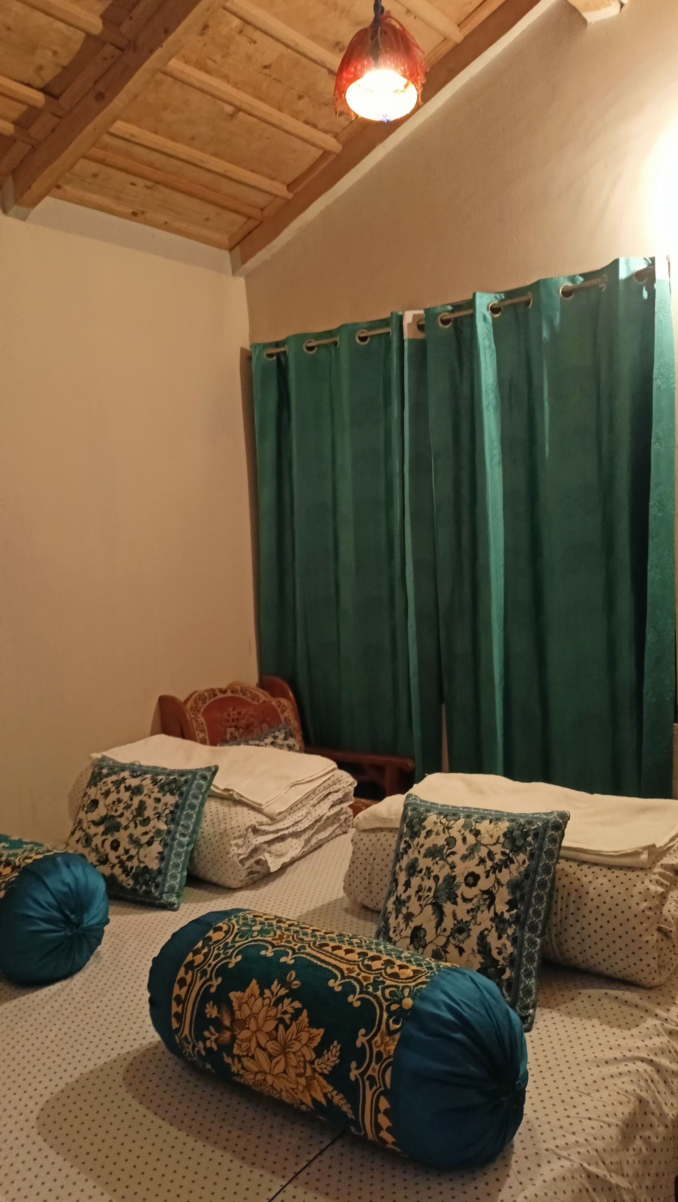 A cozy room with a wooden ceiling, a bed with patterned pillows, and a green curtain.